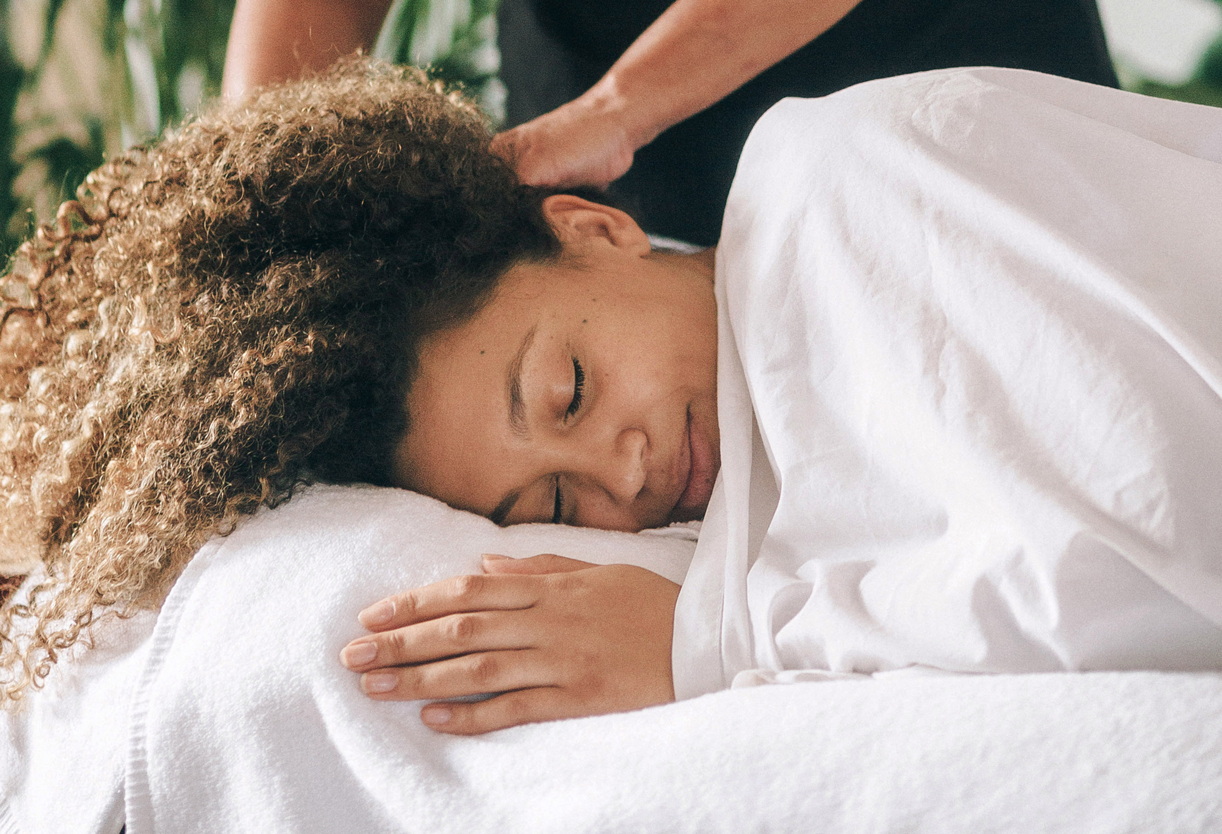 Woman lying on her side during a postnatal massage, covered by white sheet up to her face