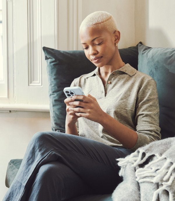 Femme assise sur un canapé, réservant un massage à domicile sur son téléphone