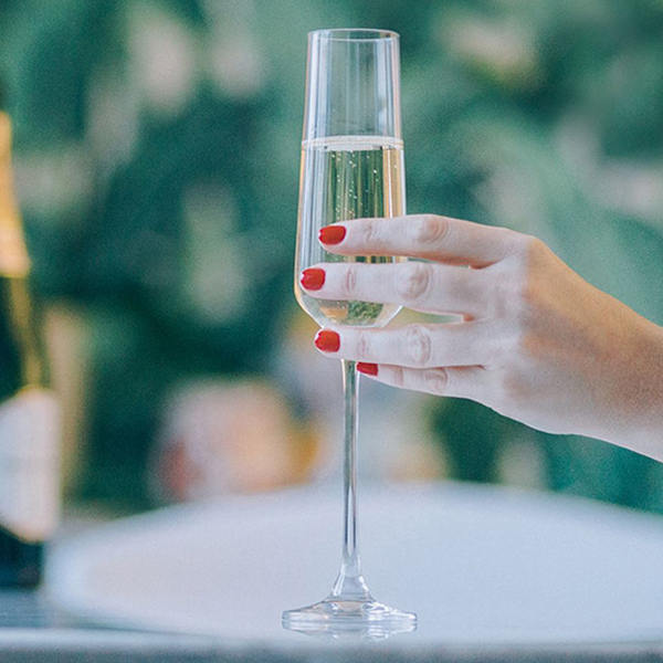 Manicured hand with red nails holding a glass of champagne