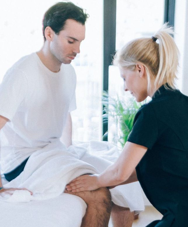 Therapist massages client's knee as he sits on massage table