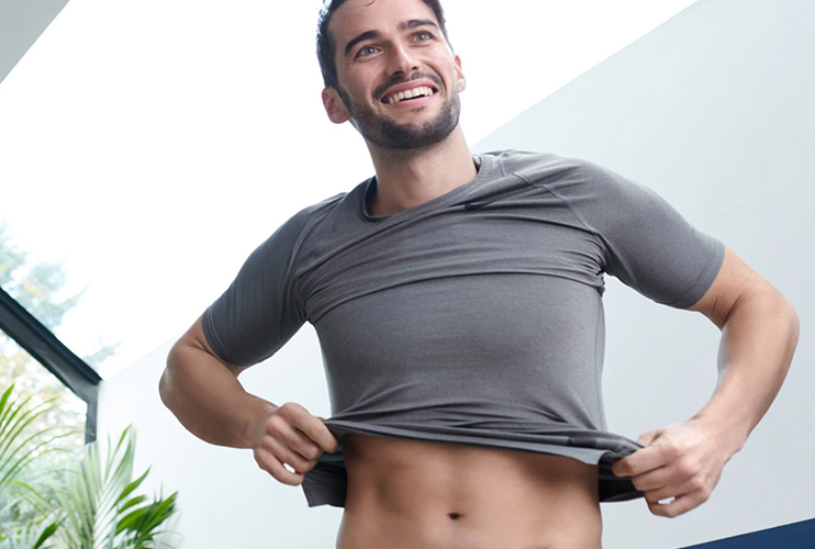 Man at home, putting on a t-shirt, with freshly waxed abs