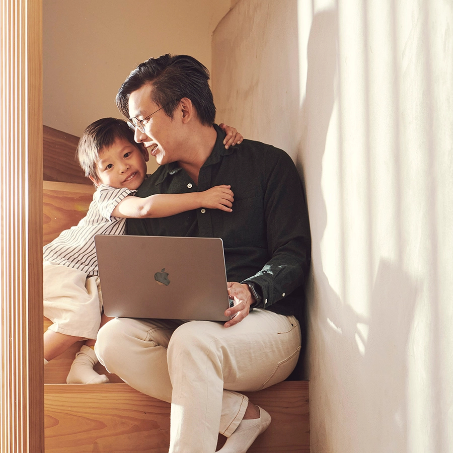 Picture of a dad being hugged by his son while working from home